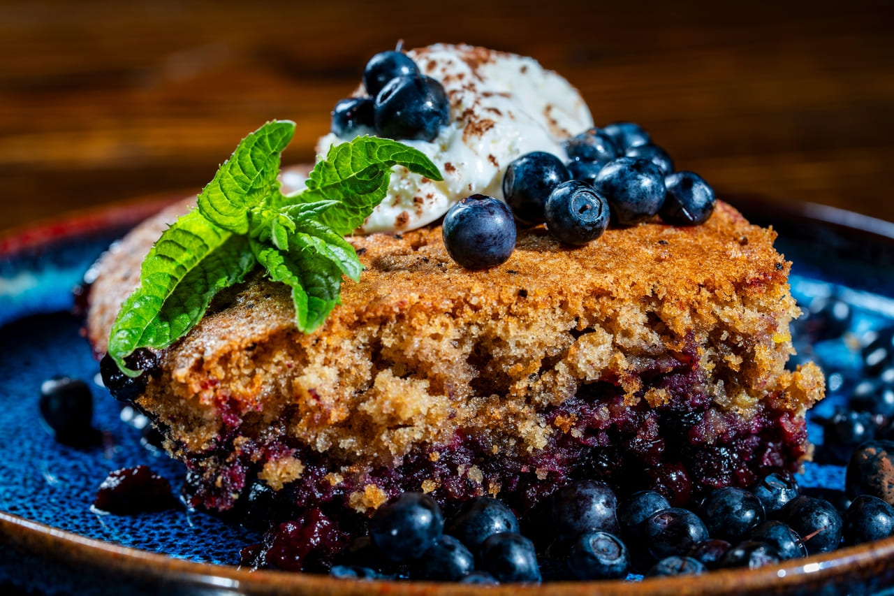 Plate with piece of fresh baked blueberry cobbler and ice cream on wooden background, close up. Homemade berry cobbler ready to eat