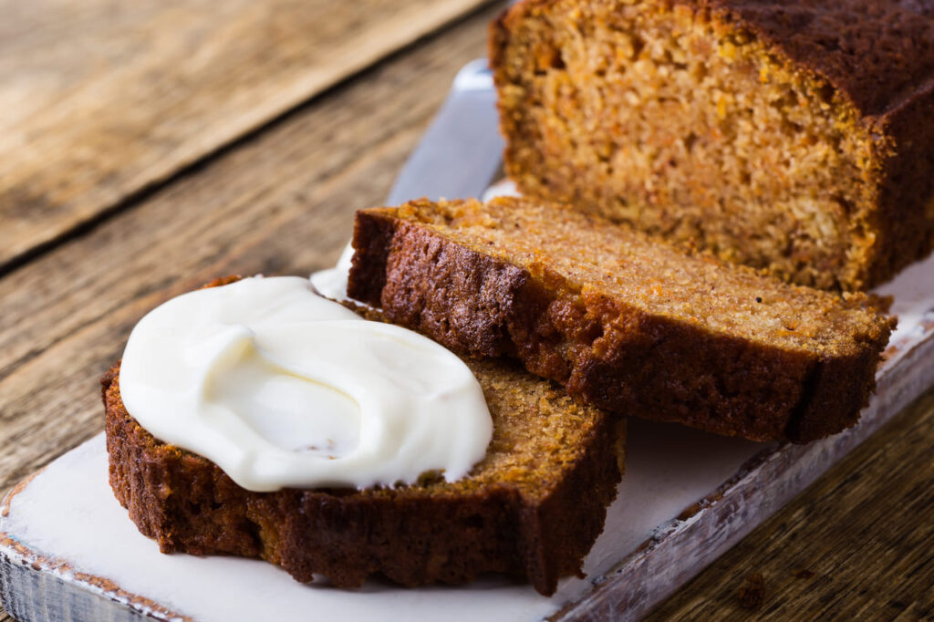 Pumpkin spice loaf sliced with cream cheese frosting spread nearby