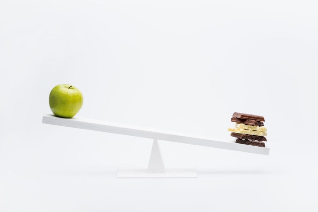 Close-up view of apple and chocolate balancing on seesaw, healthy living concept 