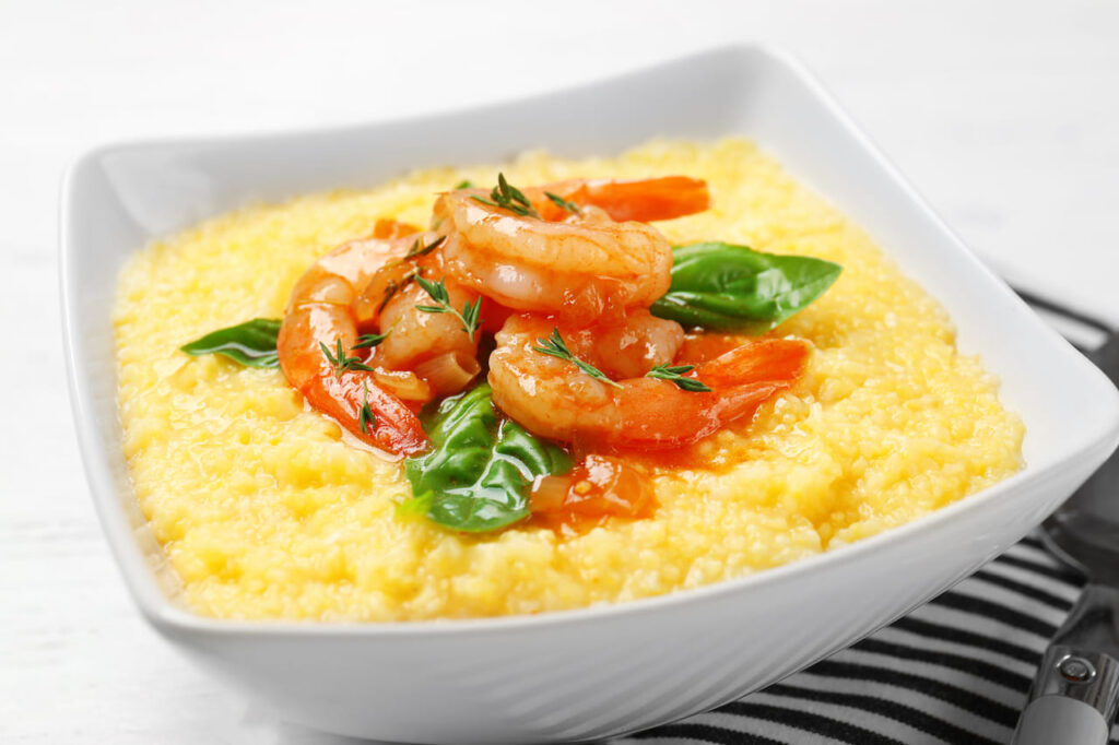 Bowl with fresh tasty shrimp and grits on table, closeup
