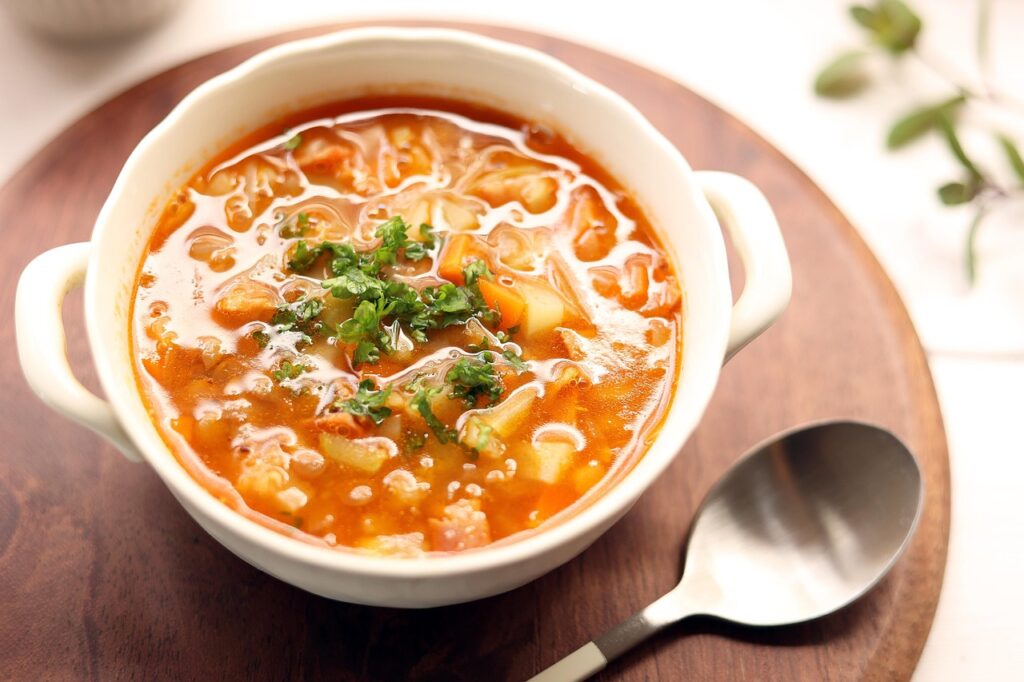 A steaming bowl of minestrone soup packed with vegetables like carrots, beans, and kale.