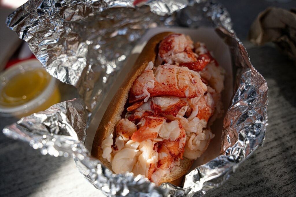 Lobster Roll: Buttered, split-top roll overflowing with lobster meat, with lemon wedges on the side.