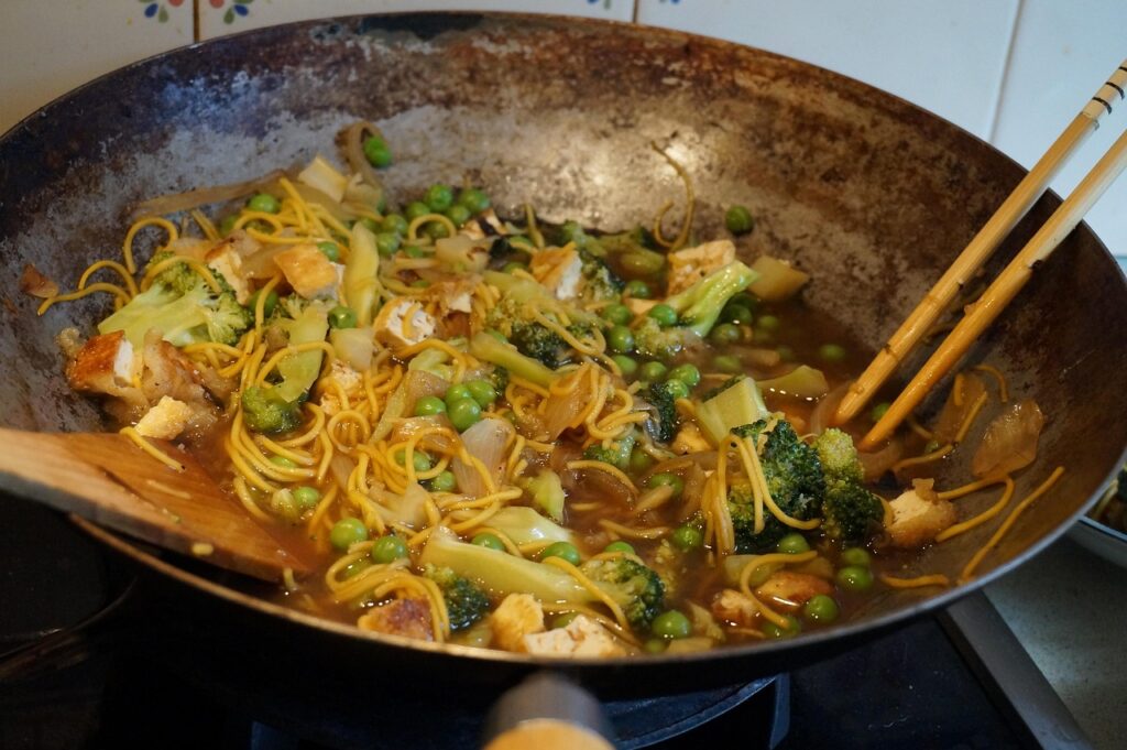 Stir-fried noodles with vegetables and soy sauce sizzling in a pan.