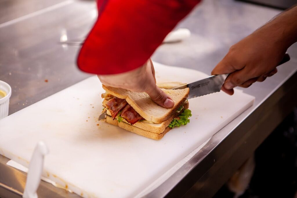 Chef cutting sandwich in rustic style with bacon and fresh vegetables