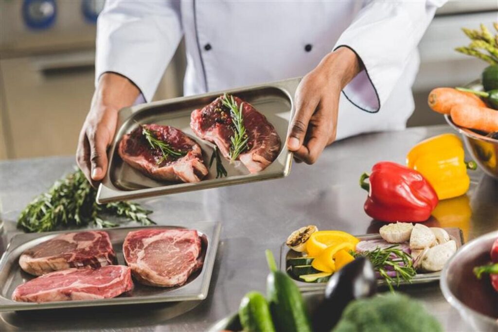 chef holding tray with raw meat at restaurant kitchen