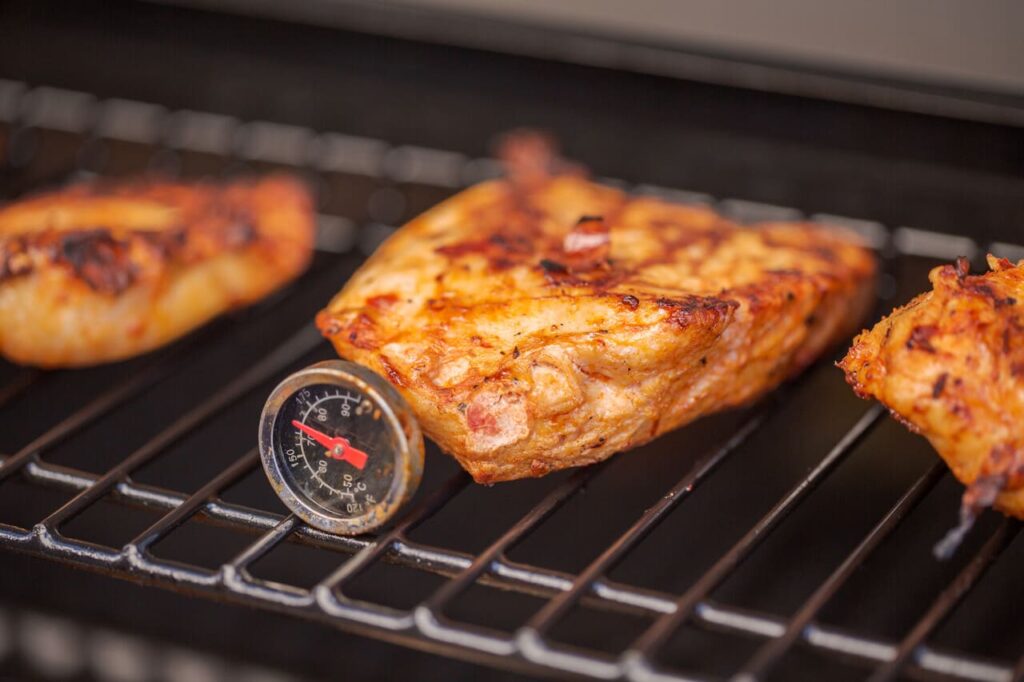 Cooking spicy chicken breasts on gas grill outdoors.
