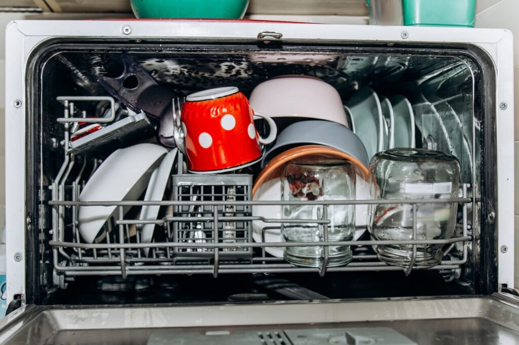 open dishwasher close up clogged with clean washed dishes.