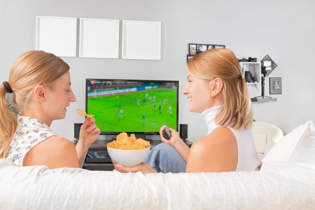 football fans watching soccer on tv sitting on couch at home.