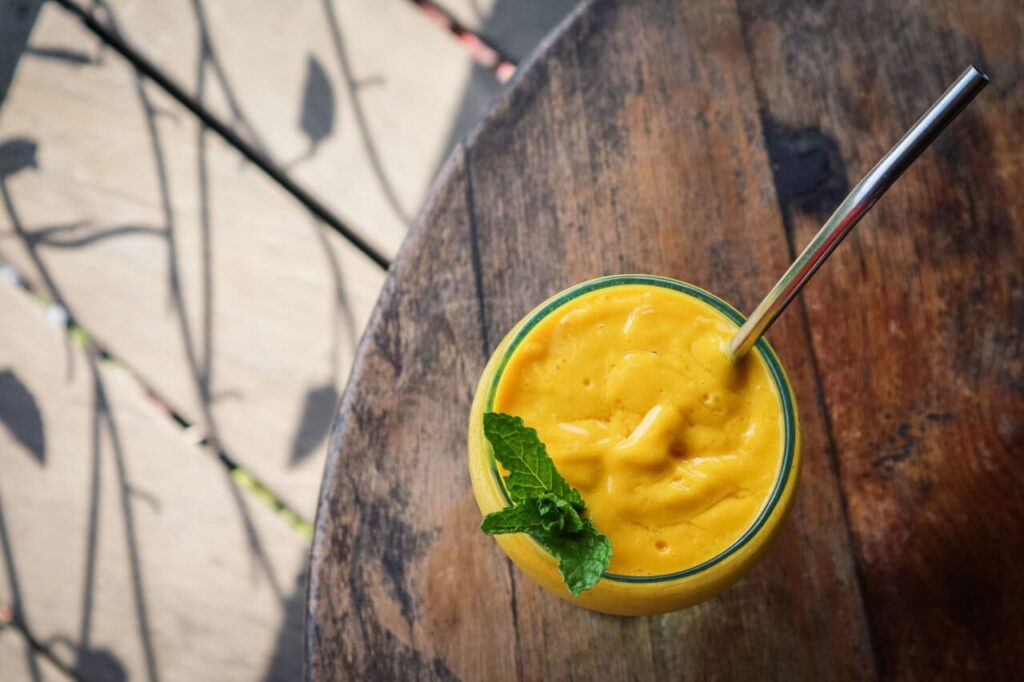 Mango juice in glass with metal drinking straw on table in tropical cafe, top view