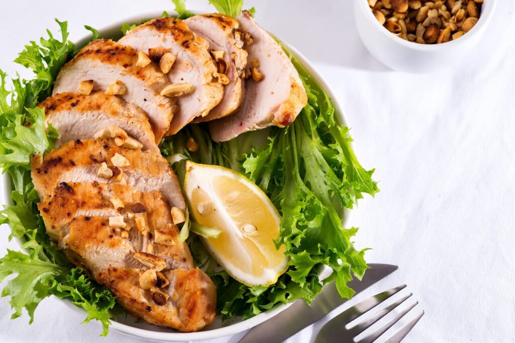 Grilled chicken breast with fresh frize salad, peanuts and lemon on a plate