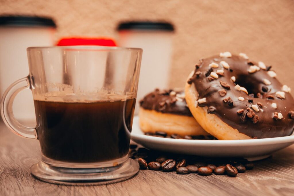 espresso and chocolate donuts on the coffee shop table with coffee grains