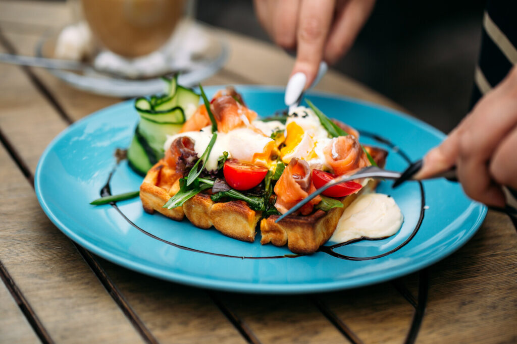 Eating waffle toast with poached egg and salmon on the wooden table