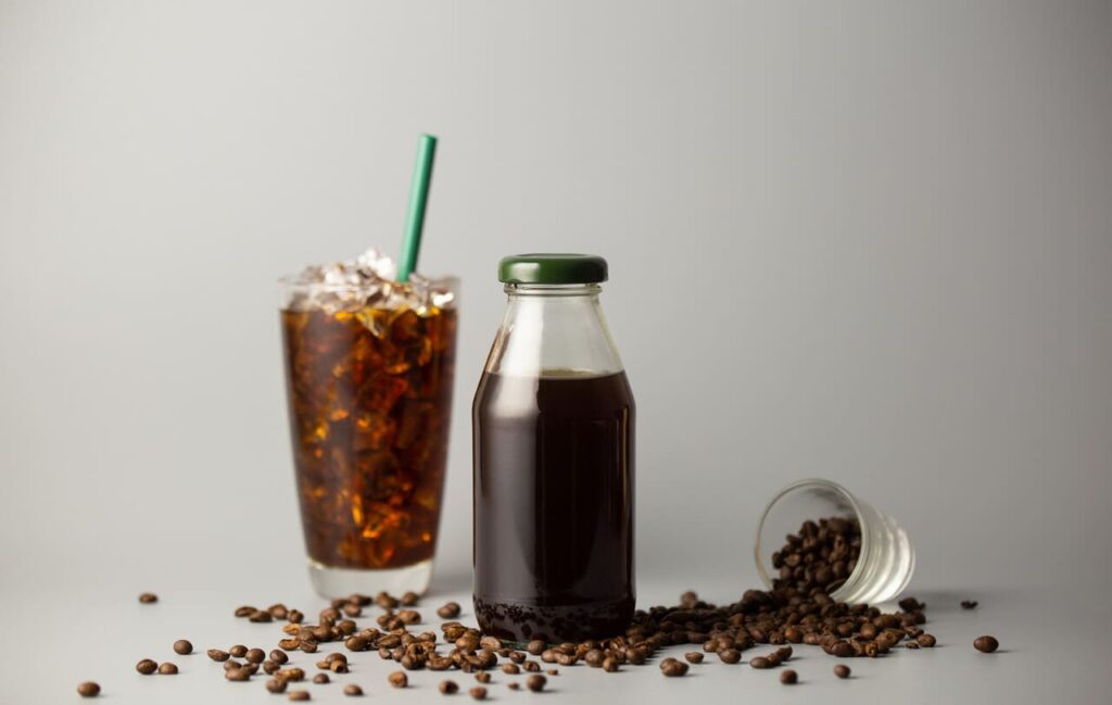 Iced americano coffee with coffee beans on grey background, Black coffee glass package for takeaway. Cold beverage product.