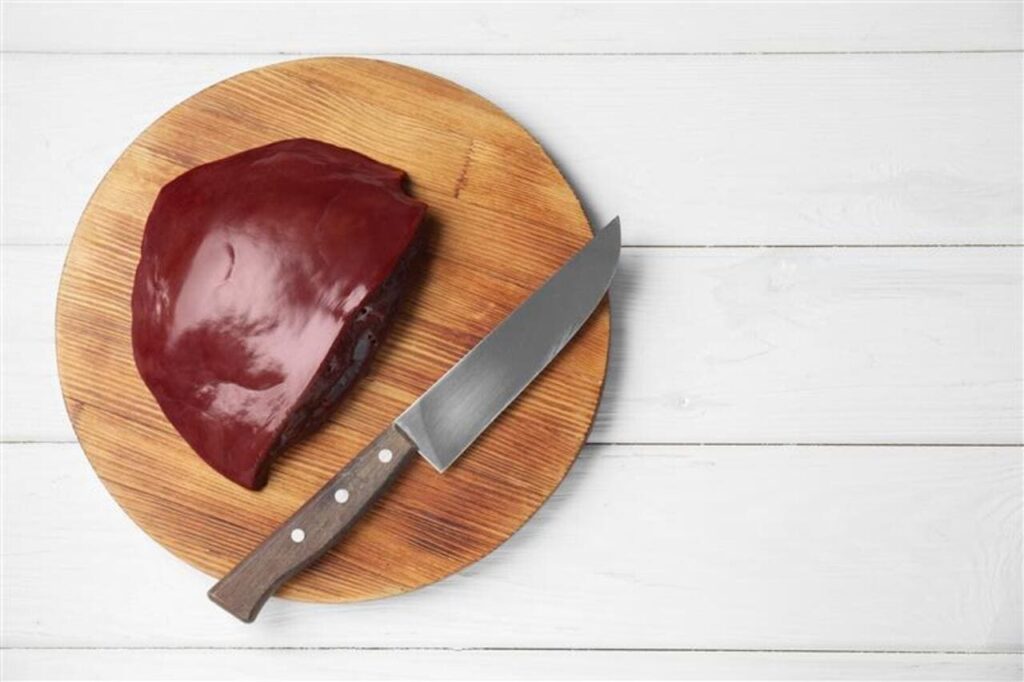 Piece of raw beef liver and knife on white wooden table, top view.