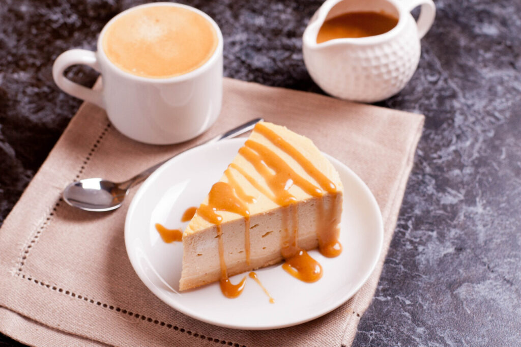 Slice of cheesecake with caramel sauce, cup of coffee on the black background,