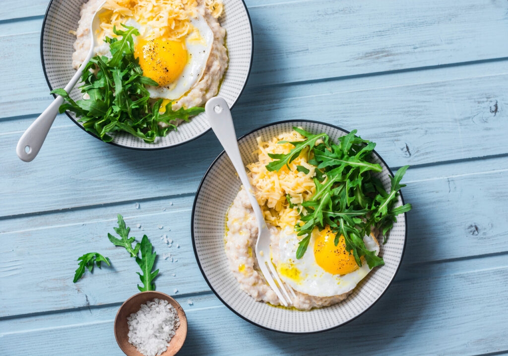 Cheese savoury oatmeal with fried egg and arugula on a blue background