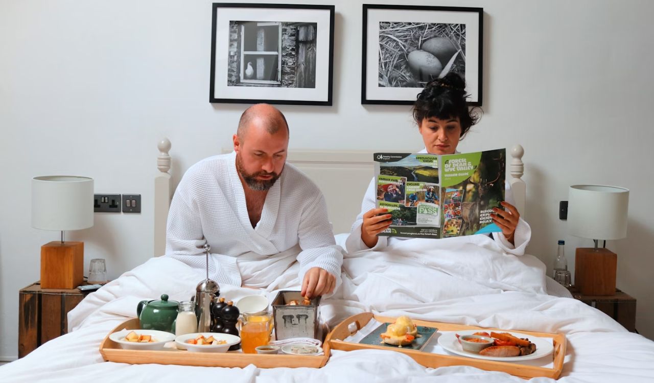A man and woman sitting on bed having breakfast