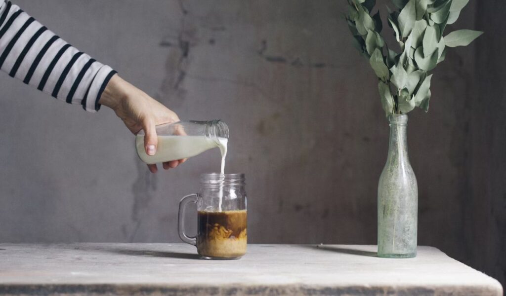 Person filling milk on glass with coffee