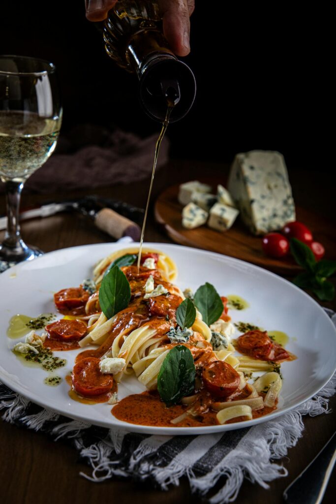 A chef pouring oil over pasta