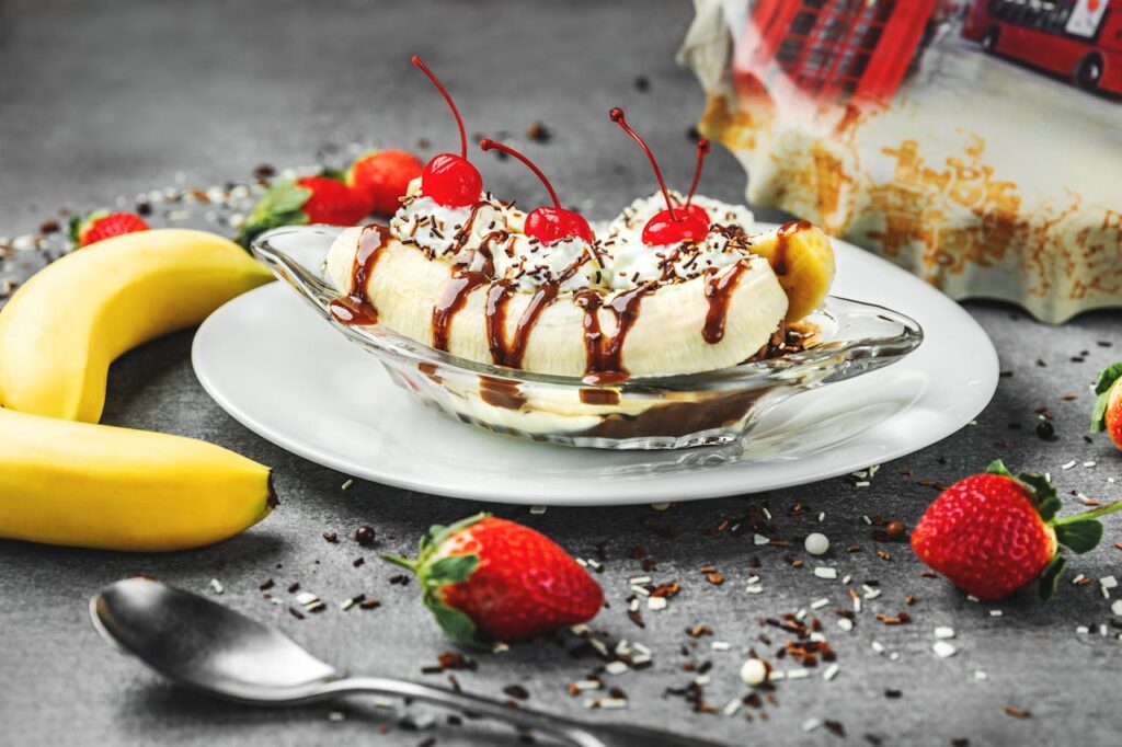 A diner-style banana split with three scoops, syrup, whipped cream, and cherries in a long dish.