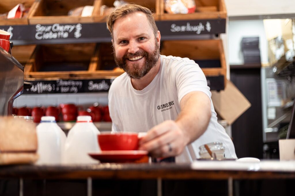 Barista smiling warmly while handing over a coffee.