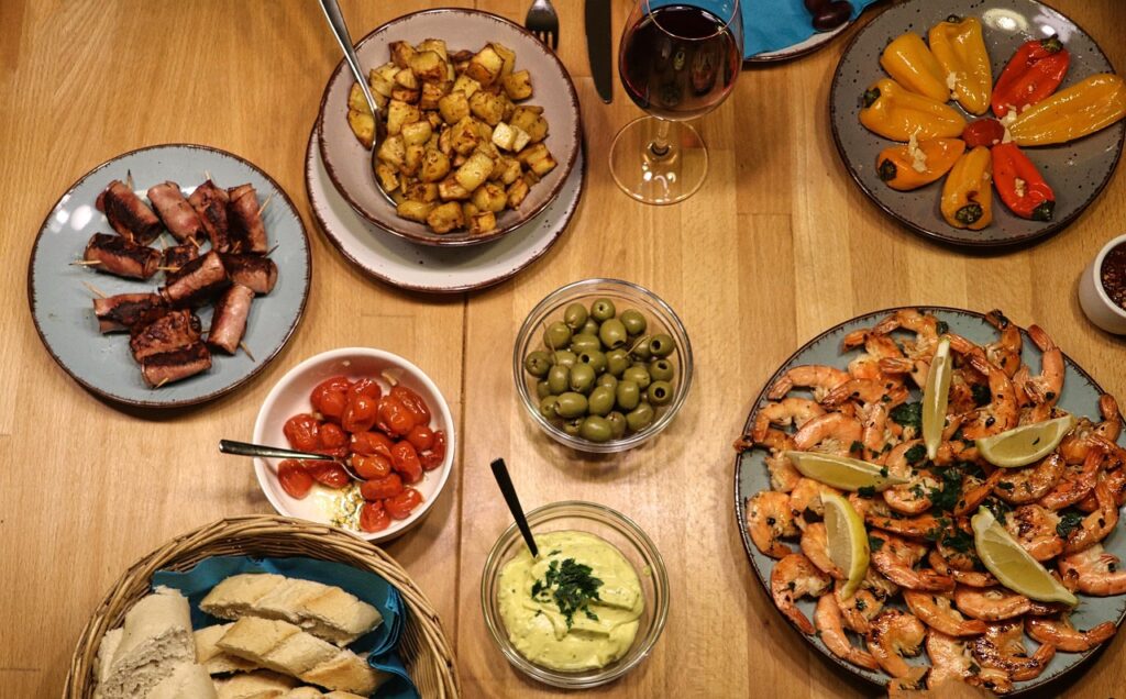 A spread of tapas plates with olives, shrimp, and potatoes served in small bowls,