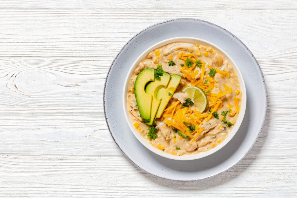 white chicken chili topped with shredded cheddar cheese, fresh slices of avocado and lime