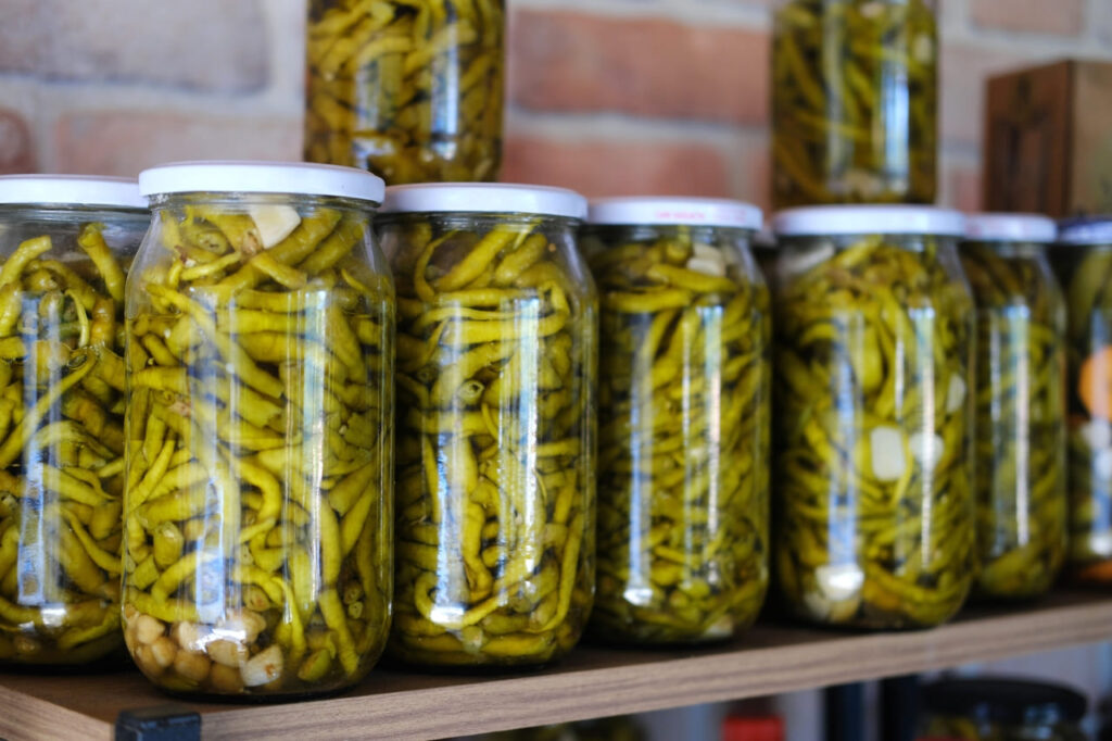 Glass jars filled with pickled green beans are lined up on a wooden shelf.