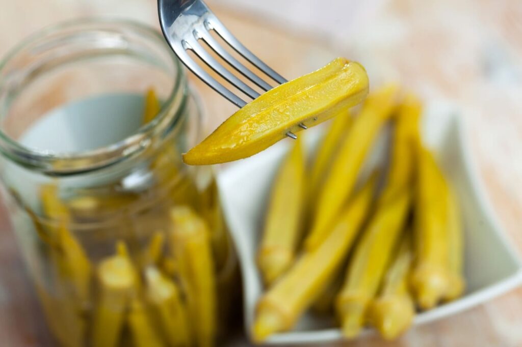 Closeup of pickled okra in a glass jar on a table in a restaurant, vegetarian food