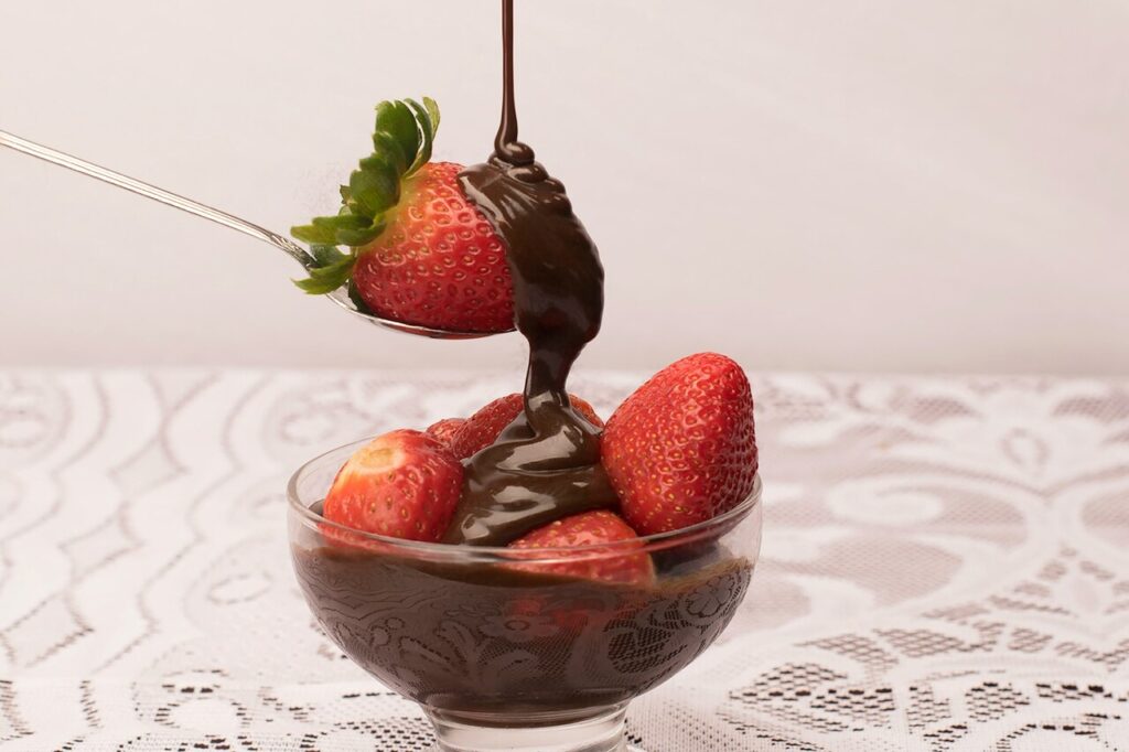  Melted chocolate dripping from a spoon over a decadent dessert, surrounded fresh berries.