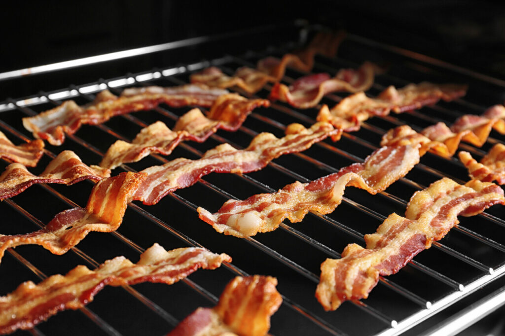 Grill with strips of bacon cooking in oven