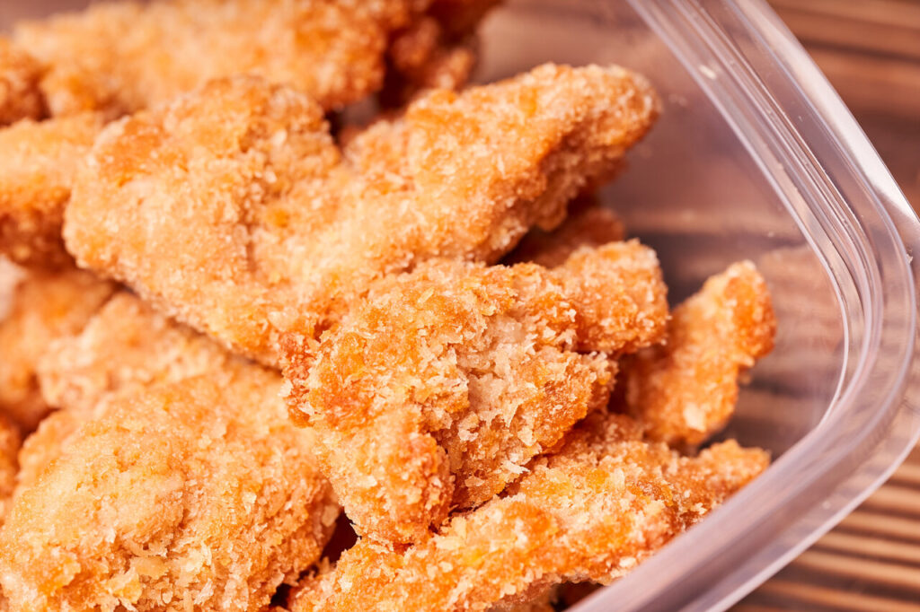 Chicken strips frozen in a plastic container on a wooden table.