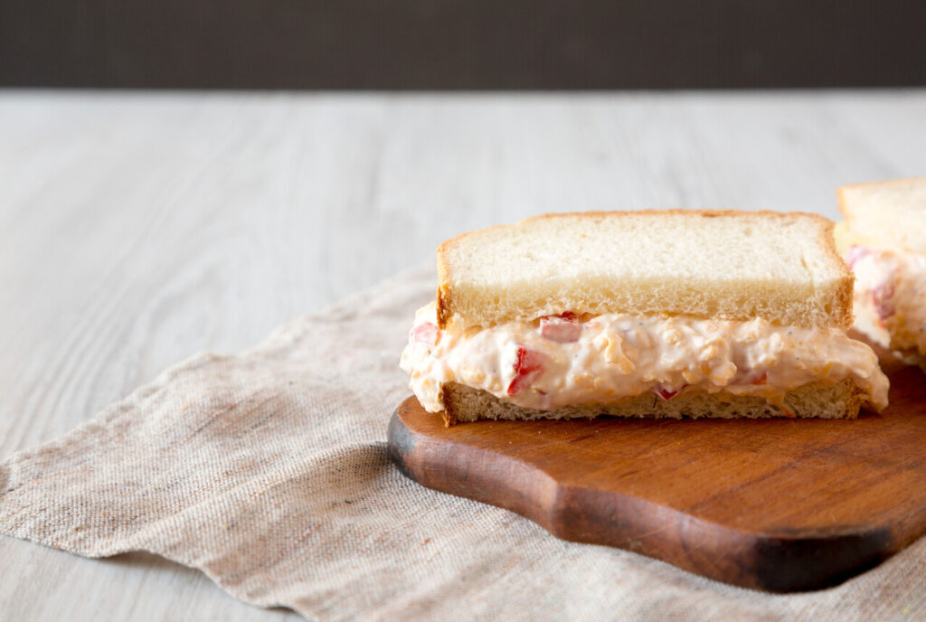 Delicious Homemade Pimento Cheese Sandwich with chips on a rustic wooden board, side view. Copy space.