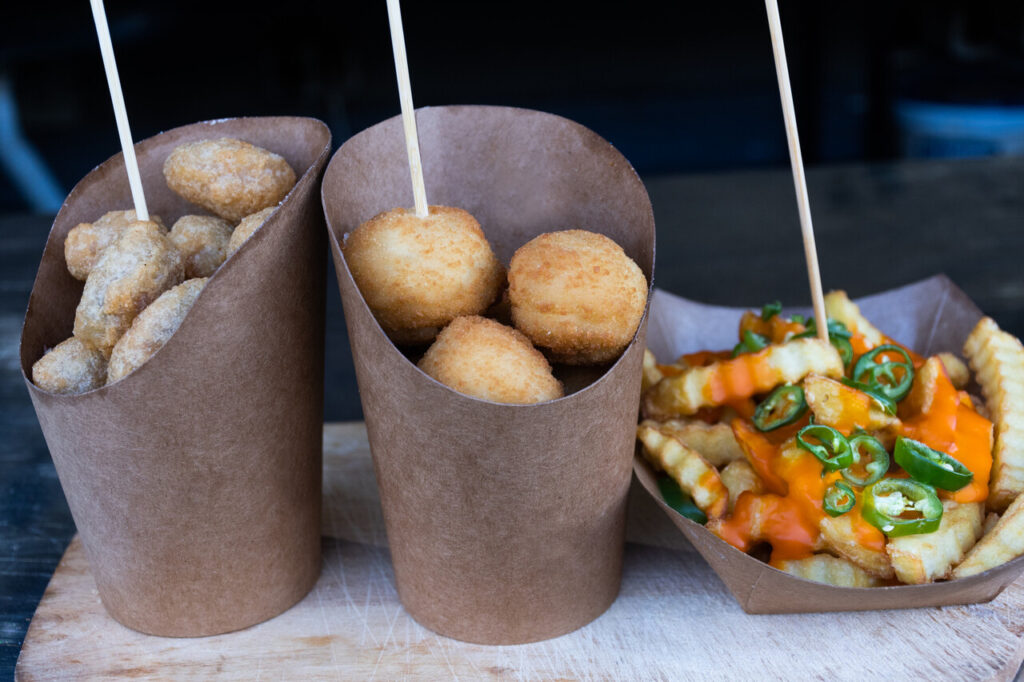 Group of Sicilian arancini in a brown paper cones and French fried potatoes with cheese cream