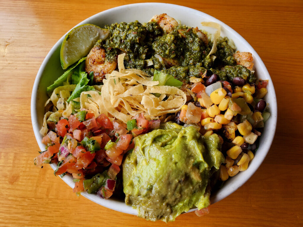 Tex-Mex shrimp salad inside a white bowl with guacamole, salsa and tortilla strips