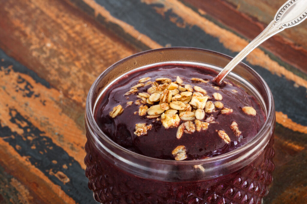 Acai pulp juice in glass with muesli spoon on wooden table