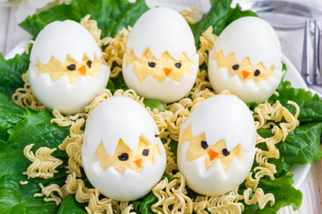 Little chicken in nest, deviled eggs served with salad and dry ramen on white plate, horizontal