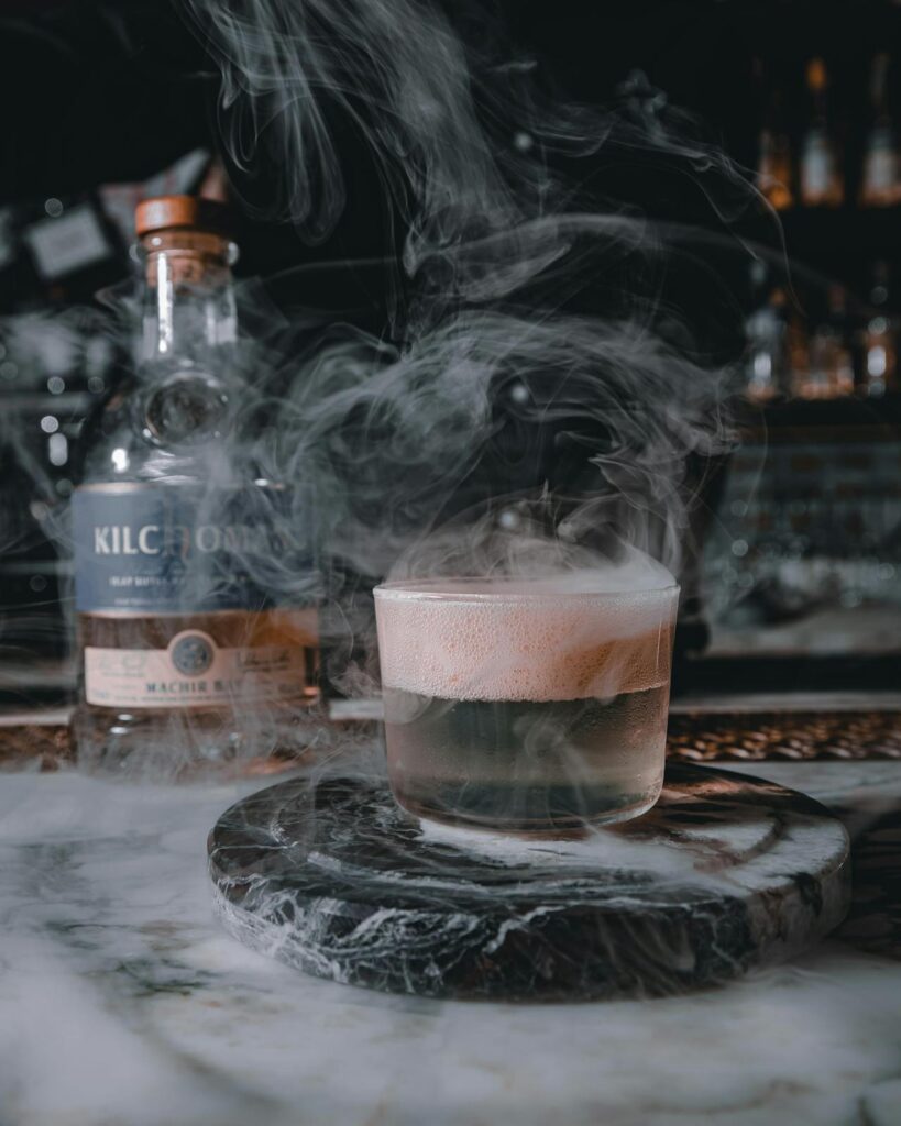 A glass of smoky whisky beside a piece of charred wood or peat brick.