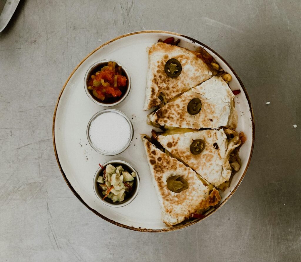 Step-by-step overhead shot of tortilla, beef, sauce, and cheese layers.
