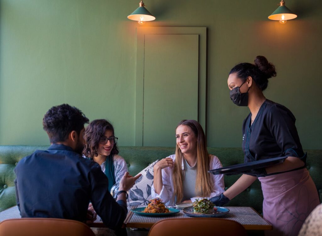 Smiling waitress serving breakfast plates to guests in a welcoming country setting.