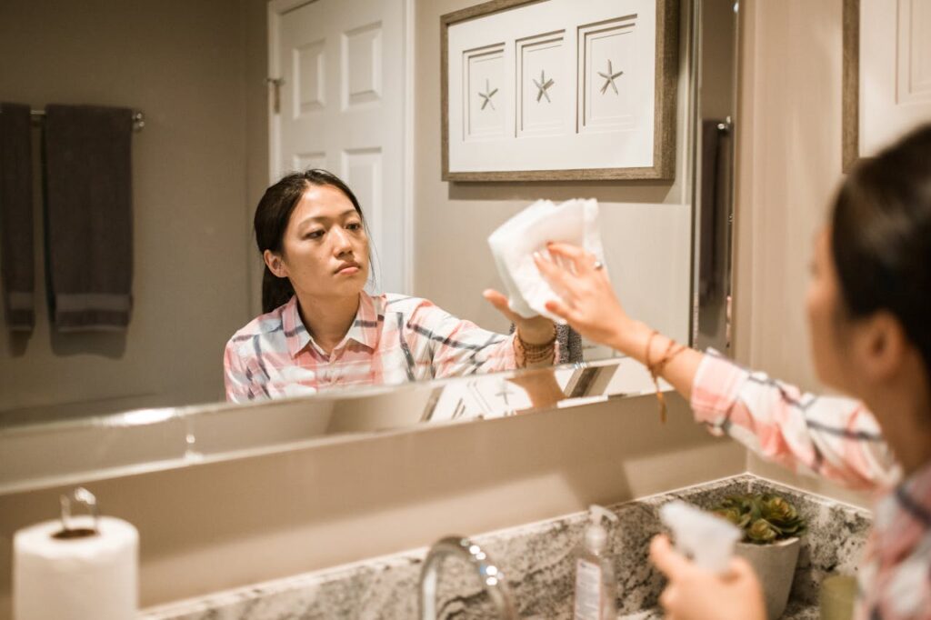 A person wiping down a bathroom sink or mirror with a cloth.