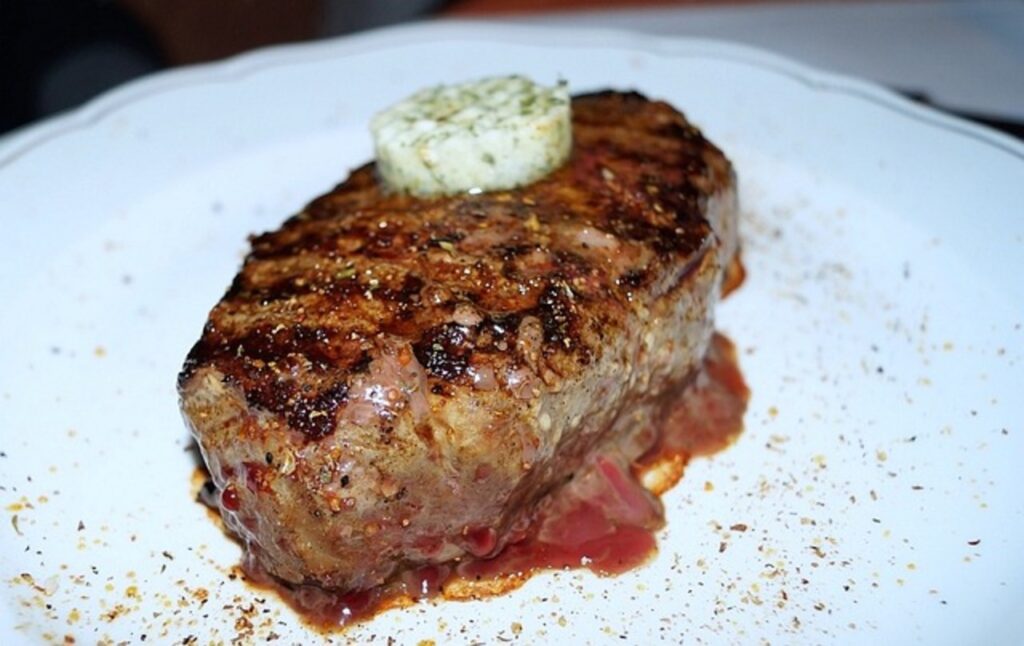 A steak topped with herb butter on a wooden board.