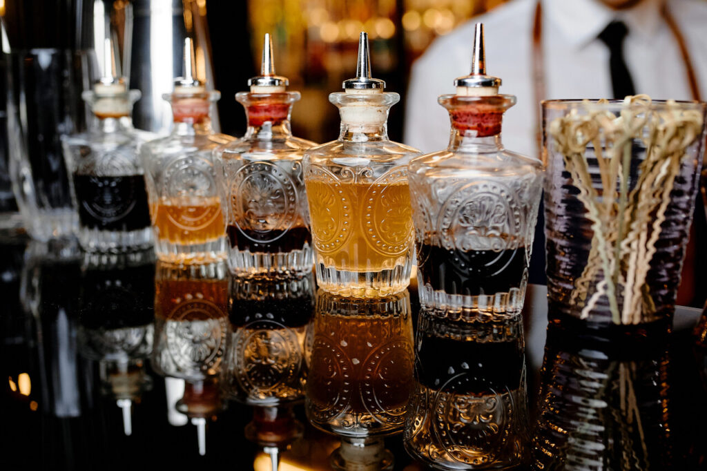different bitters bottles lined up next to a mixing glass and bar spoon