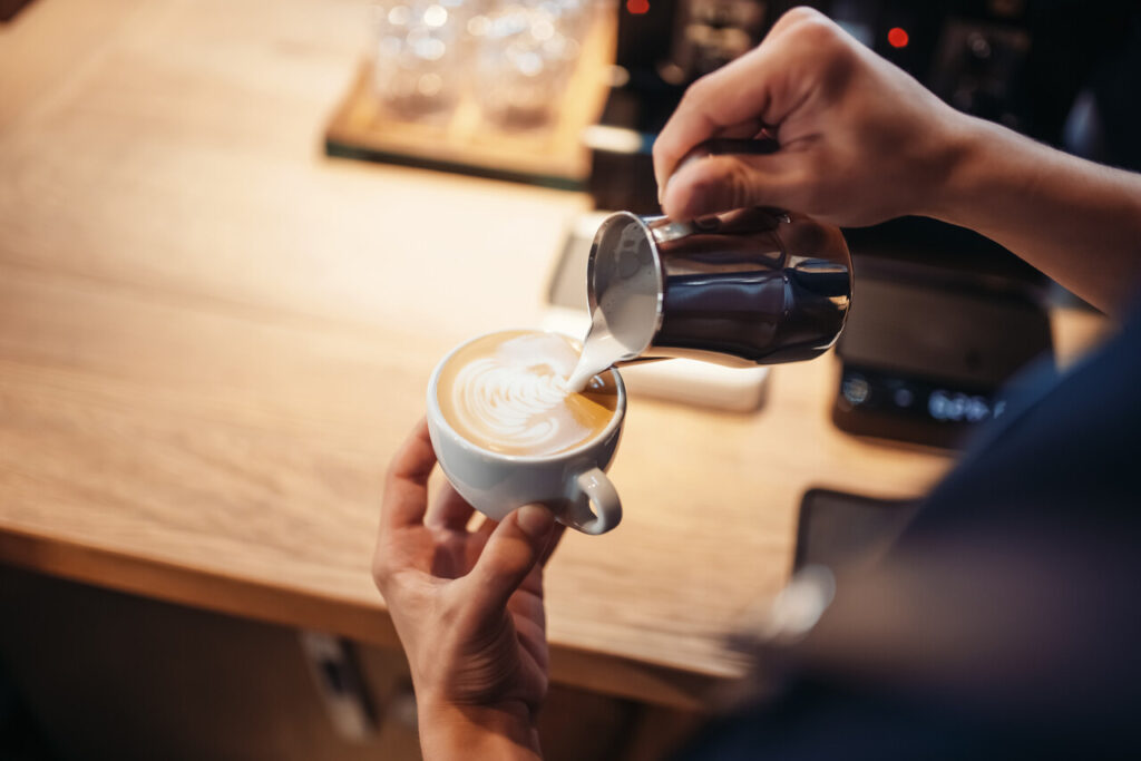 A barista pouring frothy mushroom coffee into a ceramic cup.