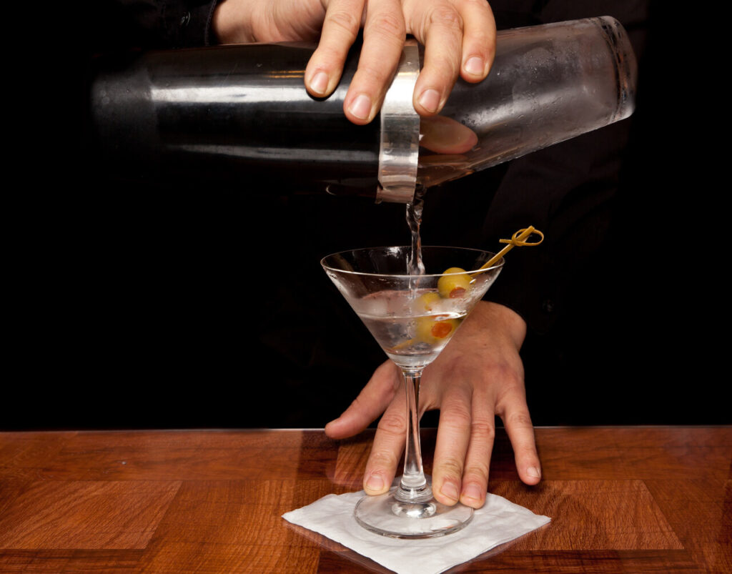 A shaker with someone pouring a martini into a glass