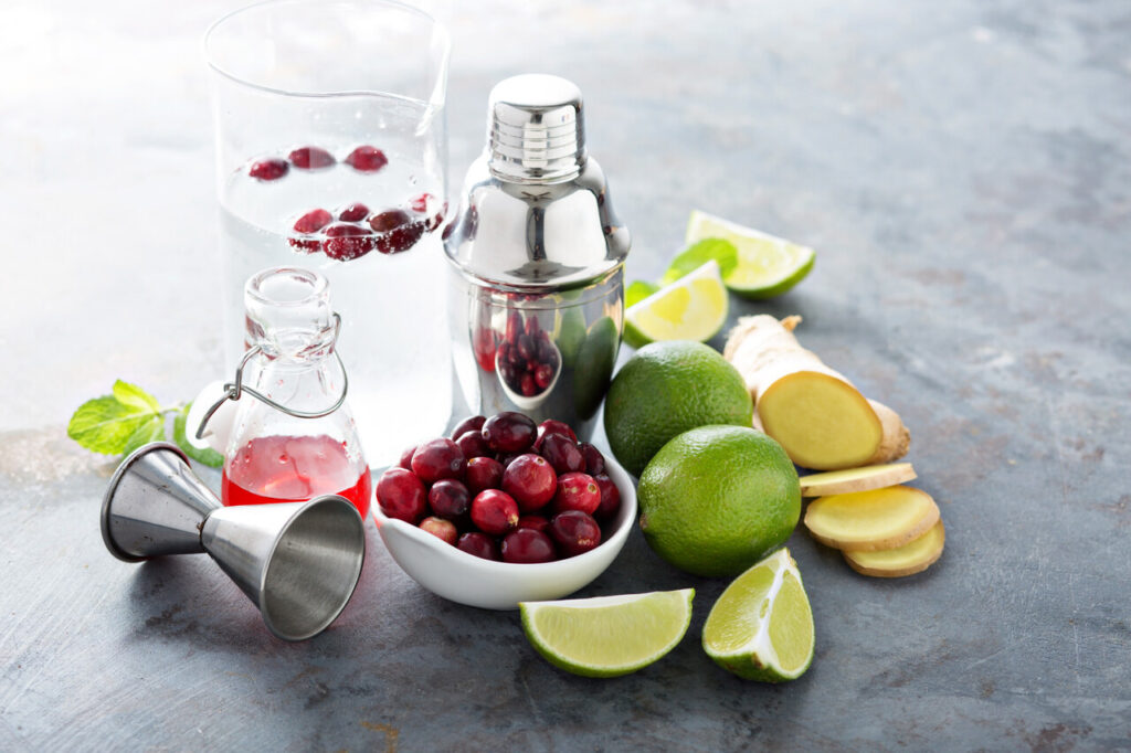 Vodka bottle, cranberry juice, lime, and cocktail ingredients laid out