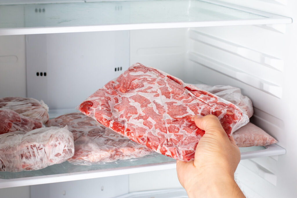 A sealed package of raw meat thawing safely on a refrigerator shelf with a tray underneath.