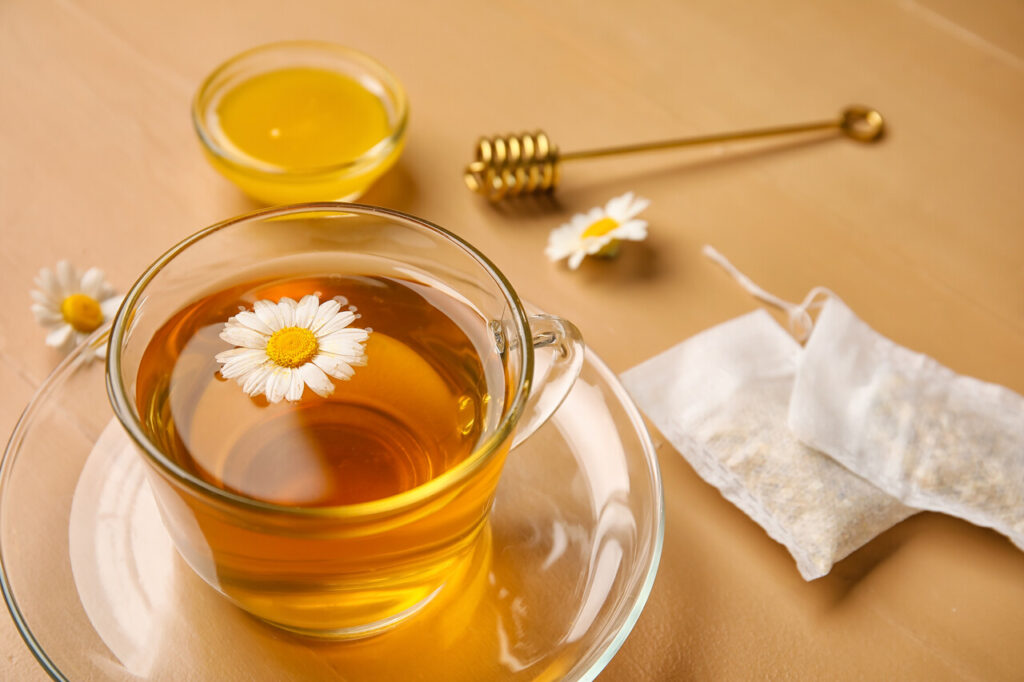 Composition with cup of chamomile tea, flowers and honey on color wooden background