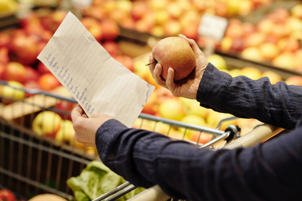 A person taking notes on a small grocery list while standing in a supermarket aisle