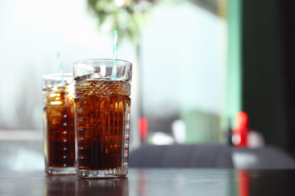 Glasses with refreshing cola and ice cubes on table indoors